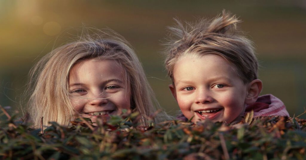 Two young girls peeking up from behind a bush