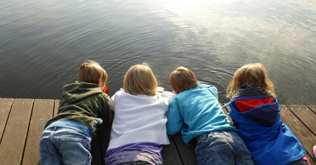 Four kids lying on a pier and watching the water