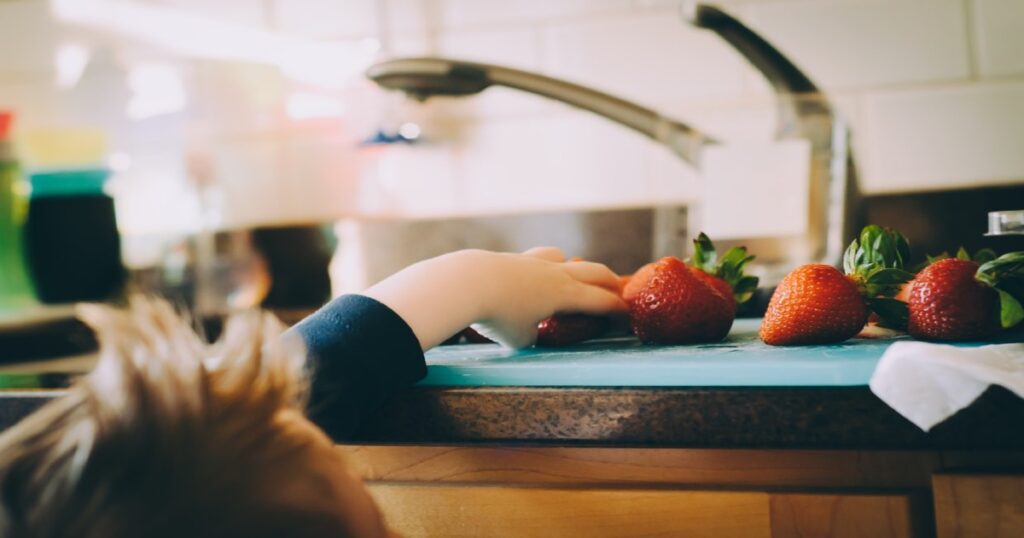 Young child reaching for strawberries on a countertop