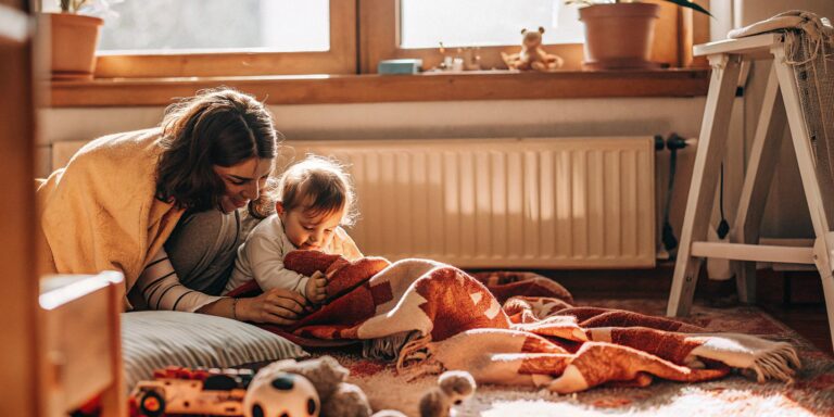 Mother and infant on the floor with toys, considering the use of an infant daycare cost calculator.