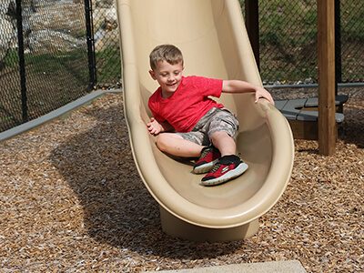 a child sliding down a slide on one of our playgrounds